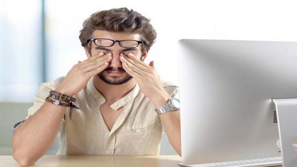Homem em frente ao computador com a mão sobre os olhos